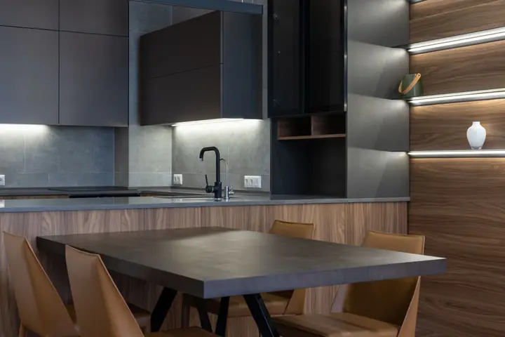 Dark kitchen cabinets with lights below and a wood table