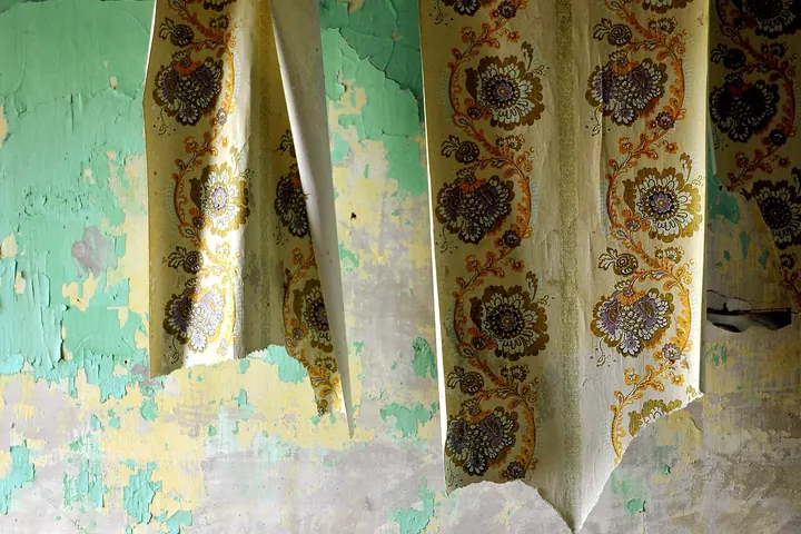 Old patterned wallpaper peeling off a plaster wall