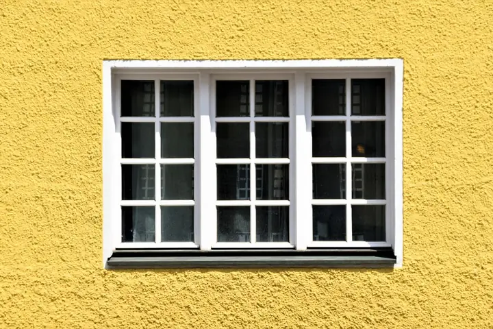 A yellow textured wall with a classic white framed window