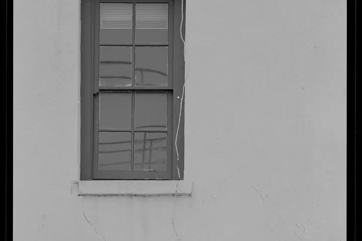 Double-hung window in a stucco wall with hairline cracks near the frame