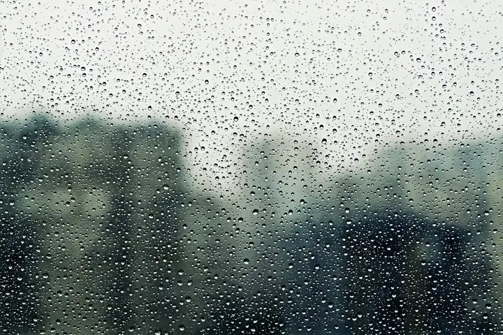 Close-up of raindrops on a window with blurred background, conveying a moody, vibe